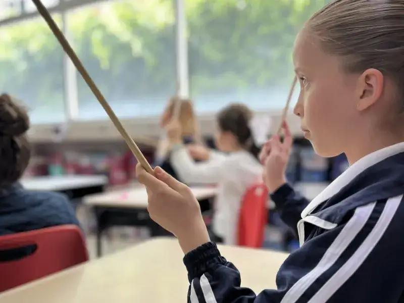 Estudiante sostiene vara mientras participa en actividad artística en aula de colegio con compañeros de clase